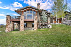 Back of house featuring stone siding, a chimney, a yard, and a wooden deck