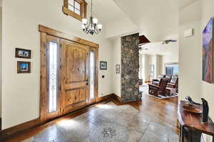 Foyer with stone tile floors, a ceiling fan, a high ceiling, and a chandelier
