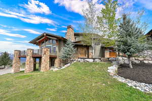 Rear view of house with stone siding, a balcony, a lawn, and a chimney