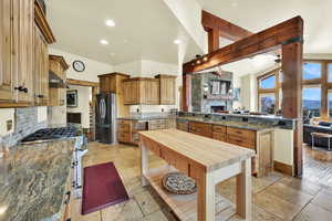 Kitchen featuring dark stone counters, wood finish cabinetry, stainless steel appliances, stone tile floors, and recessed lighting