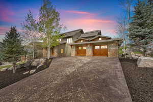 View of front facing south facade featuring stone siding, driveway, board and batten siding, and an attached garage
