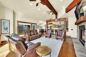 Living room with a fireplace, dark wood finished floors, beamed ceiling, a ceiling fan, and hanging lights