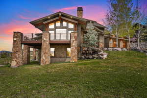 Back of house featuring stone siding, a chimney, a lawn, and a wooden deck
