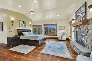 Bedroom featuring lofted ceiling, access to outside, a fireplace, wood-type flooring, and recessed lighting