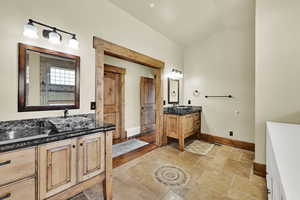 Full bathroom featuring two vanities, stone tile floors, and lofted ceiling
