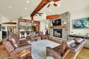 Living room with a stone fireplace, ceiling fan, recessed lighting, light wood-style floors, and vaulted ceiling