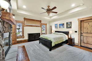 ADU Bedroom featuring a fireplace, a raised ceiling, a ceiling fan, recessed lighting, and wood finished floors