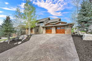 View of front facade featuring driveway, stone siding, board and batten siding, and a garage