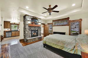 ADU Bedroom with a stone fireplace, dark wood finished floors, a ceiling fan, a raised ceiling, and recessed lighting