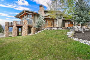 Front view of property facing south with stone siding, a yard, a balcony, and a chimney