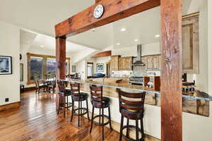 Kitchen with a kitchen bar, backsplash, light stone countertops, dark wood-type flooring, and stainless steel gas range