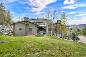 Back of house with board and batten siding, a chimney, a lawn, and a mountain view