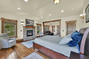 Bedroom featuring a fireplace, lofted ceiling, hardwood / wood-style floors, multiple windows, and recessed lighting