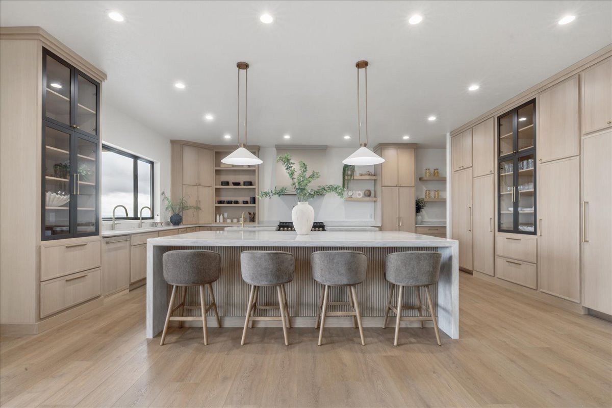 Kitchen with glass insert cabinets, a spacious island, light wood finish cabinets, and light stone counters