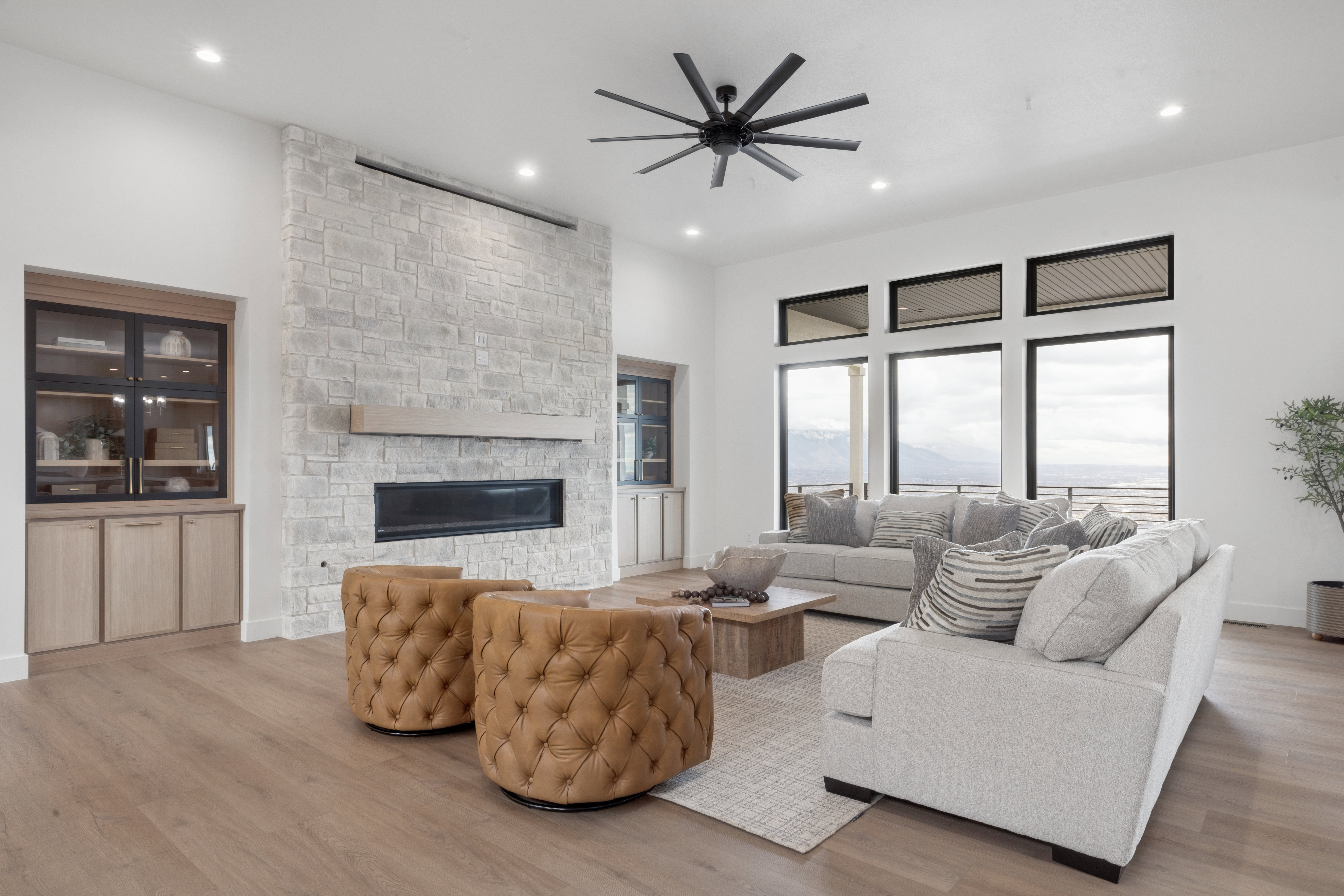 Living area with light wood-style flooring, a stone fireplace, ceiling fan, a high ceiling, and recessed lighting