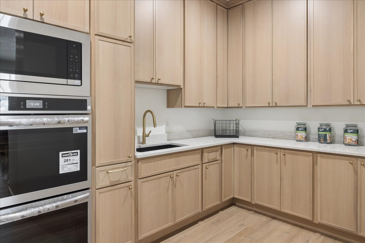Kitchen with light wood finish cabinetry, stainless steel appliances, light stone countertops, and light wood finished floors
