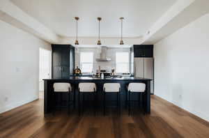Kitchen featuring dark cabinetry, decorative light fixtures, a breakfast bar, dark countertops, and a large island with sink