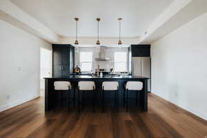 Kitchen with dark countertops, a kitchen bar, pendant lighting, dark cabinets, and a kitchen island with sink
