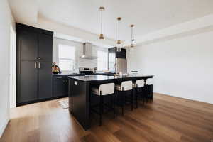 Kitchen with dark cabinets, light wood-style floors, hanging light fixtures, an island with sink, and a breakfast bar