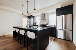 Kitchen with dark cabinets, stainless steel appliances, decorative light fixtures, dark wood-type flooring, and a center island with sink