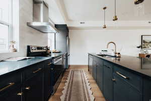 Kitchen featuring stainless steel appliances, dark cabinetry, dark stone countertops, and hanging light fixtures
