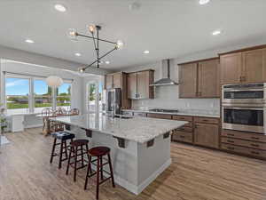 Kitchen featuring a kitchen breakfast bar, stainless steel appliances, light stone counters, light wood finished floors, and decorative light fixtures