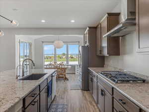 Kitchen with light wood-type flooring, stainless steel appliances, and light stone counters