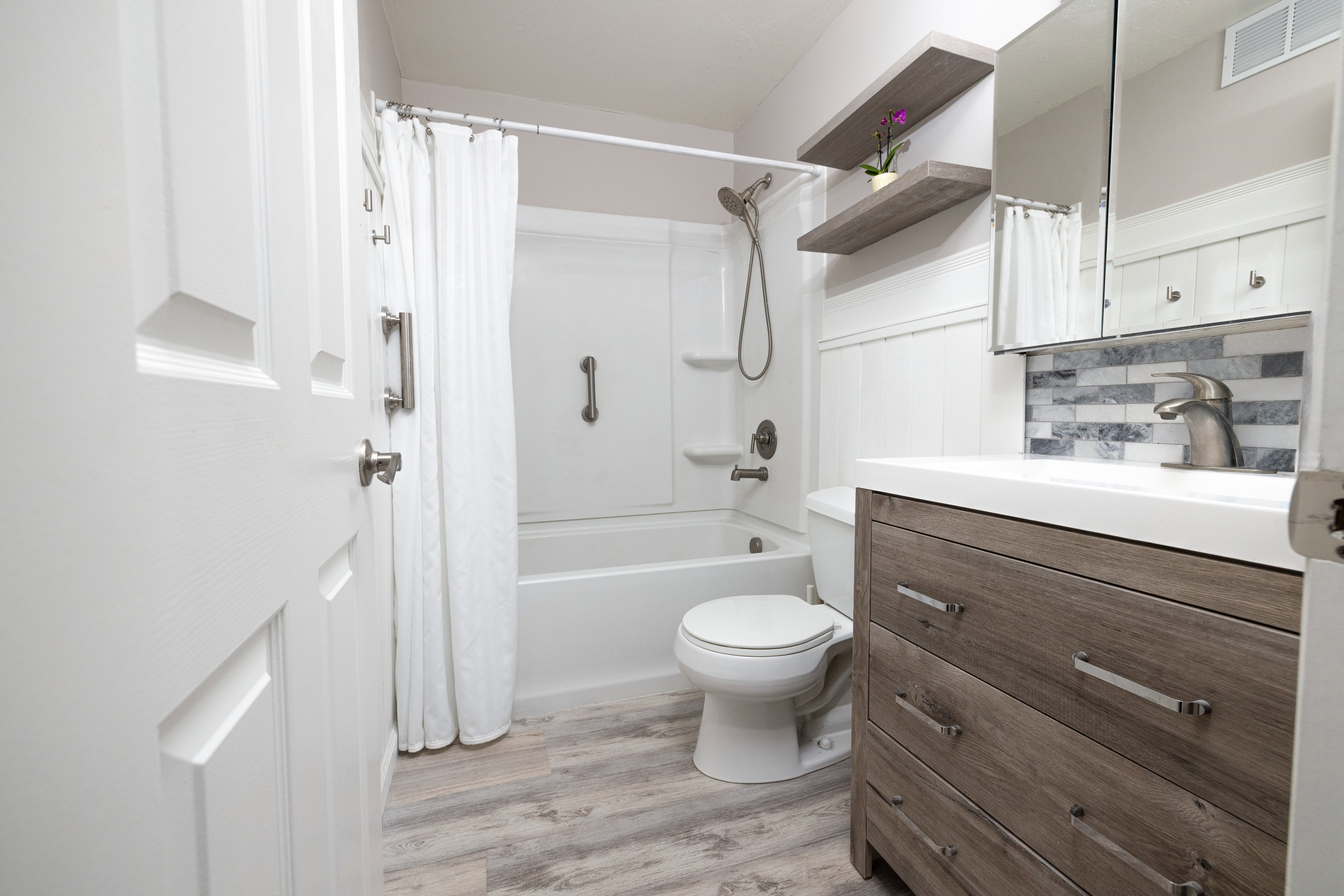 Bathroom featuring vanity, light wood-type flooring, shower / bathtub combination with curtain, and decorative backsplash