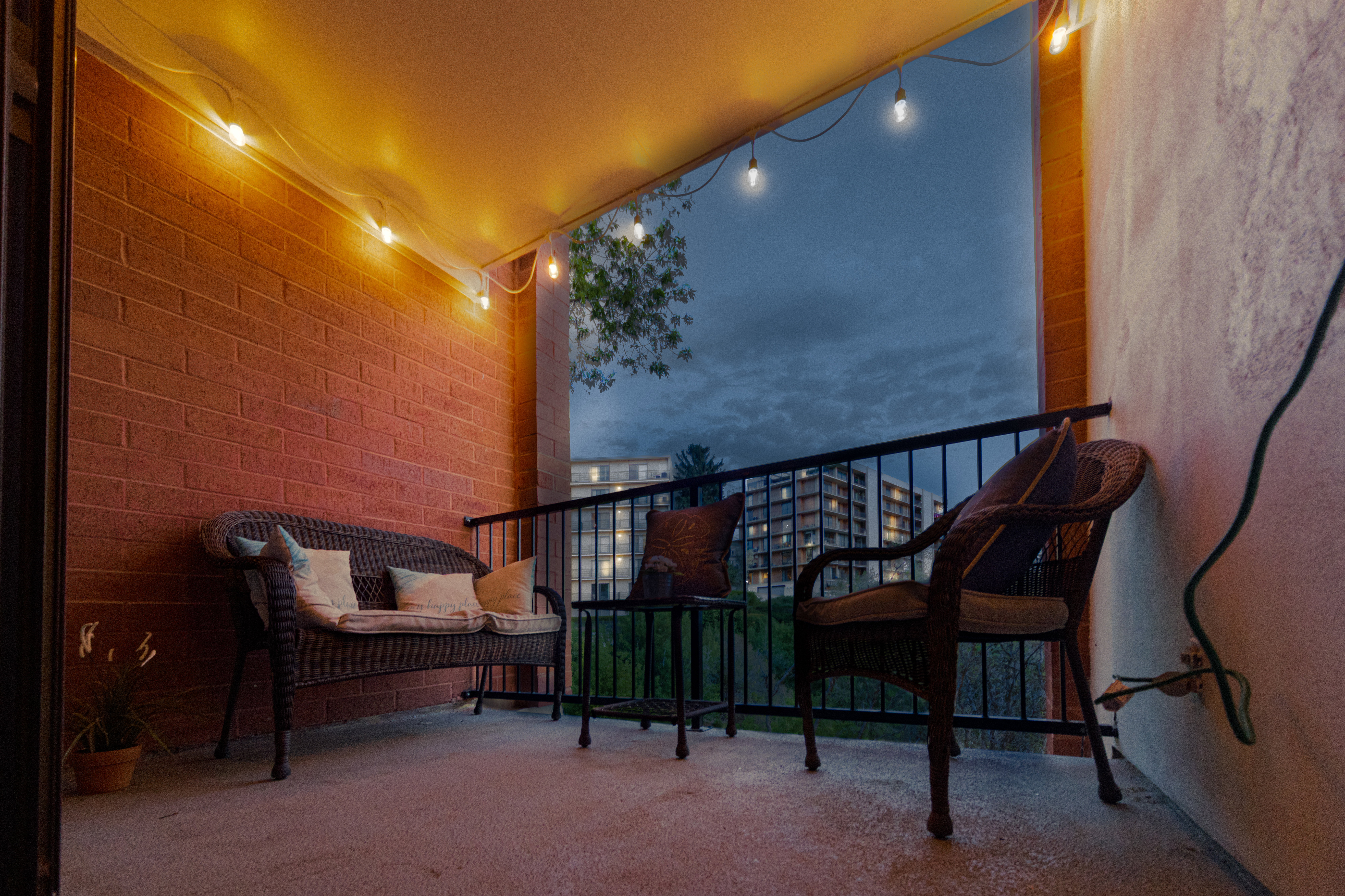 Private outdoor balcony with concrete flooring, a brick exterior wall, and a black metal railing