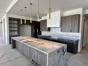 Kitchen featuring modern cabinets, a spacious island, pendant lighting, dark wood finish cabinets, and decorative backsplash