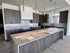 Kitchen with modern cabinets, light stone counters, tasteful backsplash, dark wood finish cabinetry, and a center island