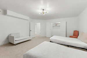 Bedroom with light colored carpet, a closet, a textured ceiling, and hanging lights