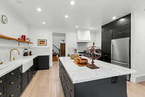 Kitchen featuring dark cabinetry, light stone countertops, decorative backsplash, a center island, and recessed lighting