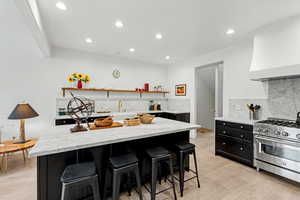 Kitchen with dark cabinetry, light stone counters, high end stove, decorative backsplash, and a breakfast bar