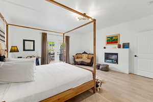 Bedroom featuring french doors, a glass covered fireplace, light wood-style floors, and access to exterior