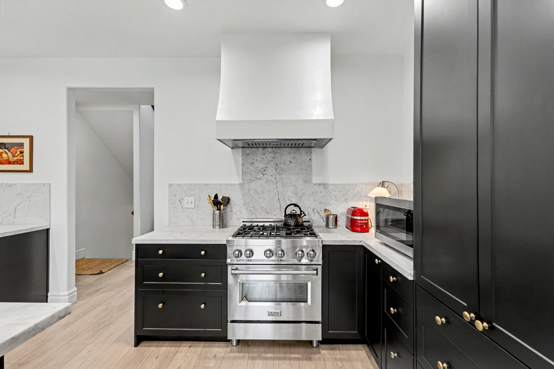 Kitchen featuring dark cabinets, stainless steel appliances, light stone countertops, tasteful backsplash, and light wood-type flooring