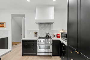 Kitchen featuring dark cabinets, stainless steel appliances, light stone countertops, tasteful backsplash, and light wood-type flooring