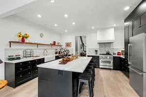 Kitchen featuring dark cabinetry, high end appliances, light stone countertops, a breakfast bar, and a kitchen island