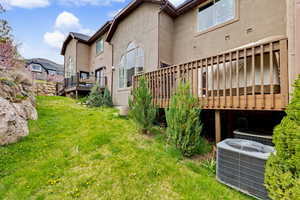 Rear view of house with a wooden deck, stucco siding, and a lawn