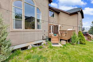 Rear view of house featuring a wooden deck, stucco siding, a yard, and a shingled roof