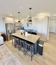 Kitchen featuring decorative light fixtures, stainless steel appliances, a kitchen bar, light wood finished floors, and an island with sink