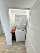Laundry area with stacked washer and clothes dryer and light wood-style floors