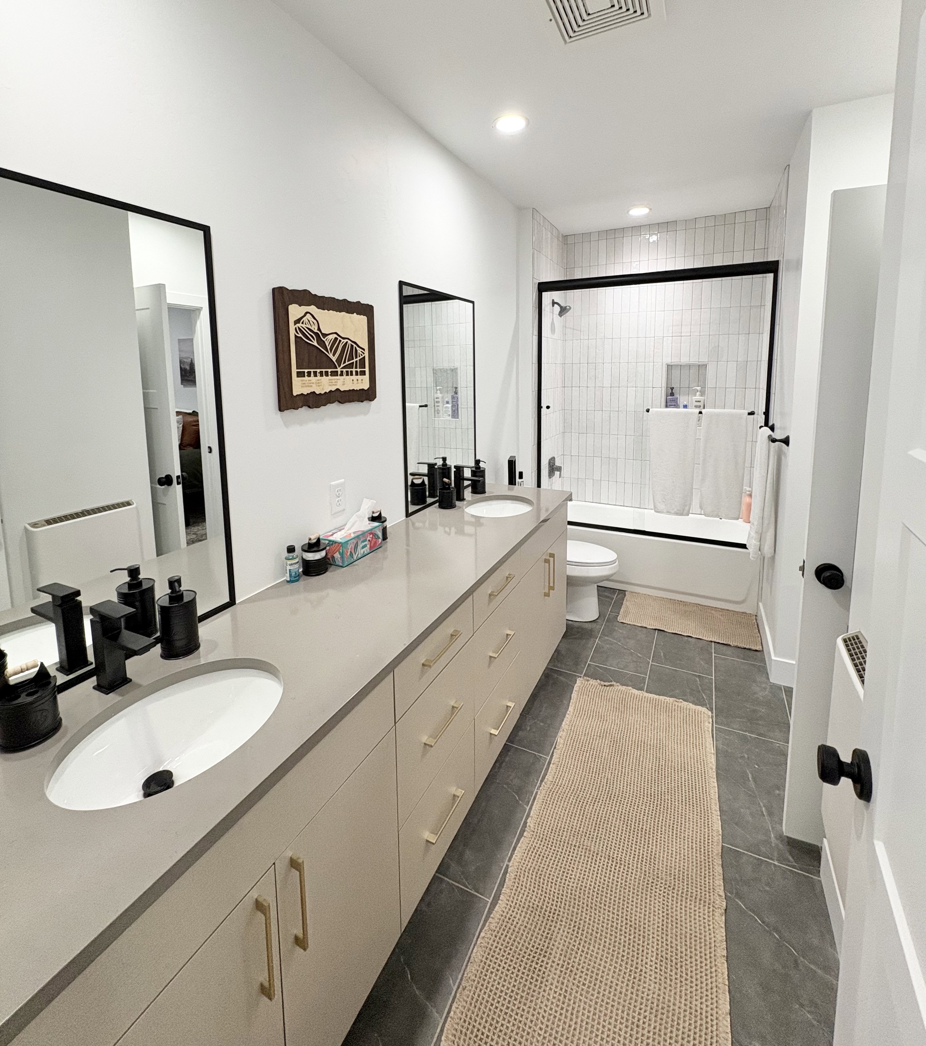 Full bathroom with double vanity, enclosed tub / shower combo, recessed lighting, and dark tile patterned flooring