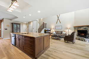 Kitchen with light stone countertops, open floor plan, a center island with sink, light wood finished floors, and recessed lighting