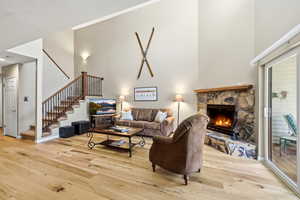 Living room featuring light wood finished floors, a stone fireplace, and a high ceiling