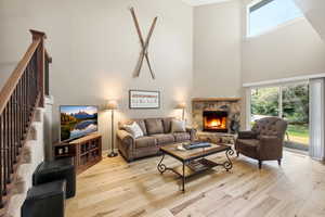 Living room with hardwood / wood-style floors, a stone fireplace, and a high ceiling