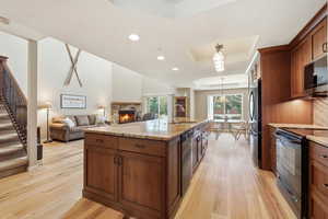Kitchen with a raised ceiling, black appliances, wood finish cabinetry, and light stone counters