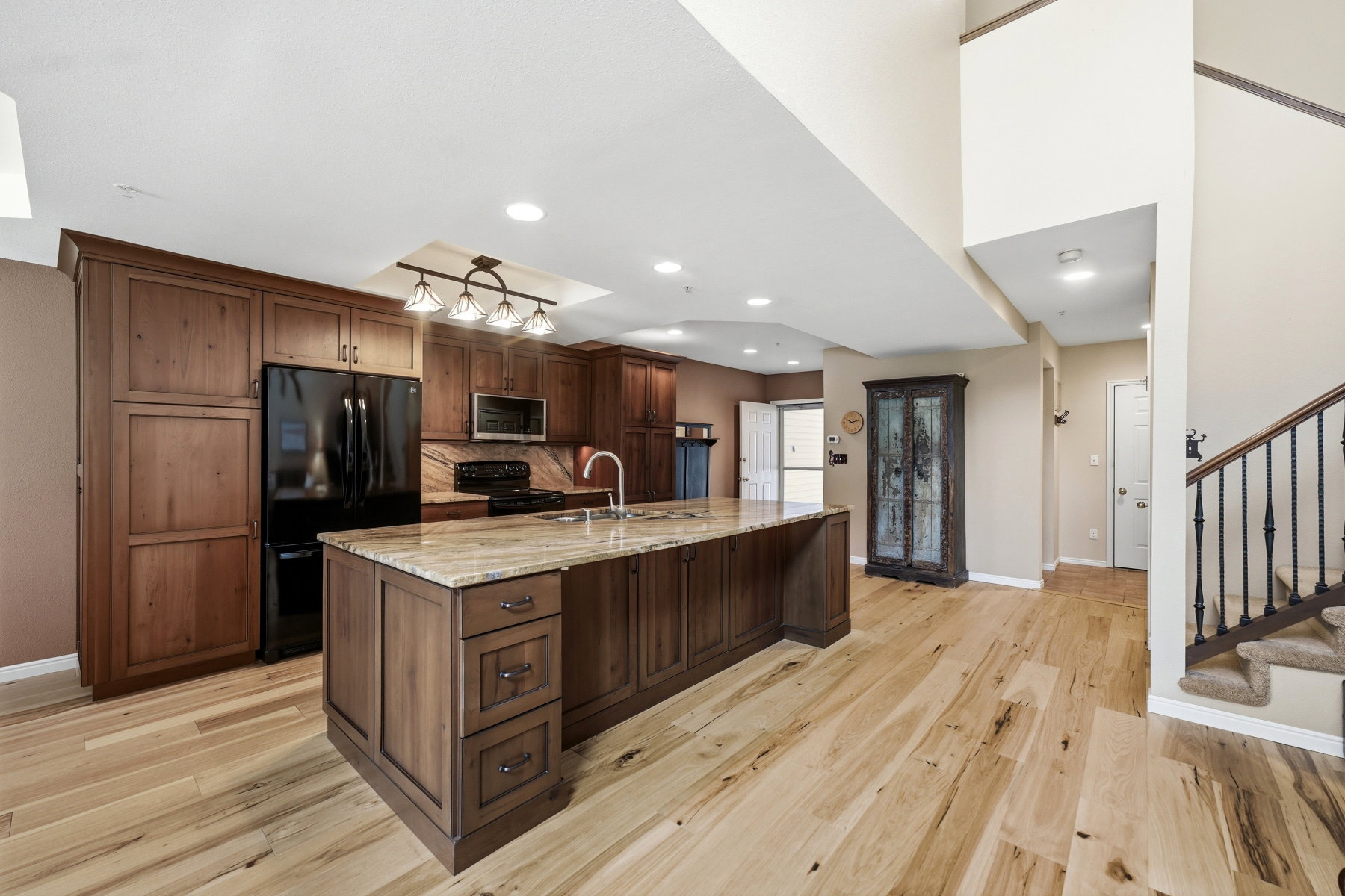 Kitchen with black appliances, light stone countertops, a large island with sink, light wood-style floors, and tasteful backsplash
