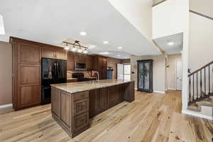Kitchen with black appliances, light stone countertops, a large island with sink, light wood-style floors, and tasteful backsplash