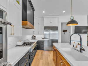 Two tone kitchen with dual tone cabinetry, light wood-type flooring, stainless steel appliances, light stone counters, and hanging light fixtures